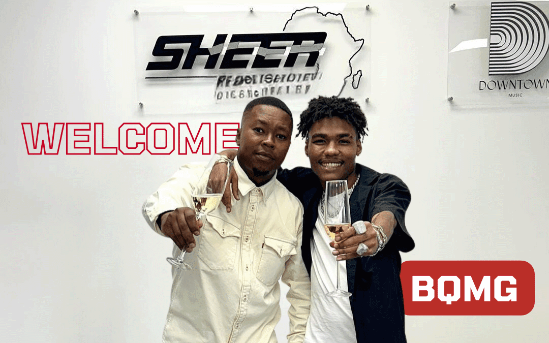 Two smiling men stand side by side, holding champagne glasses in a celebratory toast. They are in front of signs for Sheer Publishing Africa and Downtown Music. The word “WELCOME” and a red BQMG logo appear on the wall behind them.