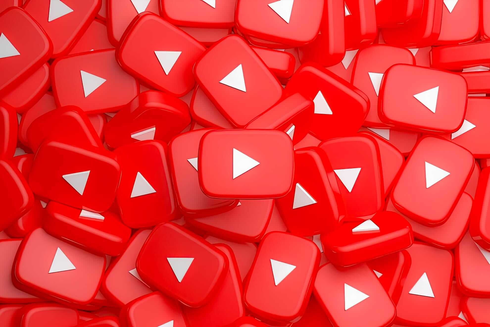 A pile of glossy, red, rectangular buttons featuring the white YouTube play icon. The buttons overlap each other, filling the entire frame and creating a vibrant, bold pattern dominated by the red and white colours.