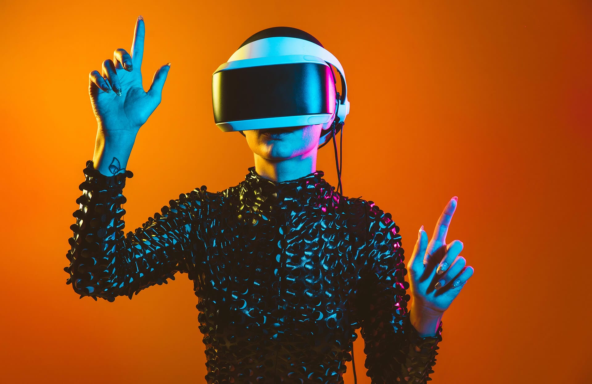 A person in a spiky black textured outfit and a virtual reality headset stands against an orange gradient background, raising both hands with index fingers up, as if exploring AI music tools in an immersive virtual environment.